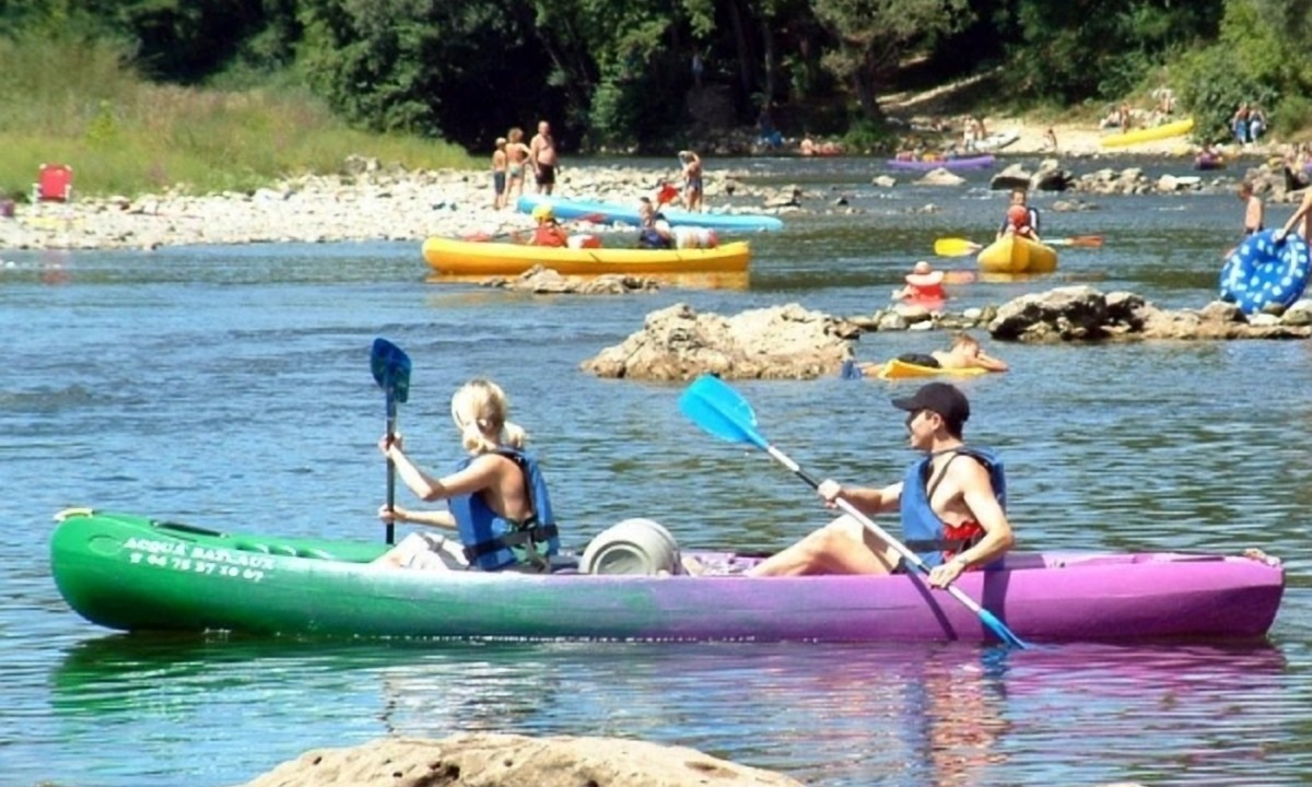 At Les Ranchisses, two individuals paddle a vibrant kayak on a river encircled by other kayakers and lush greenery.