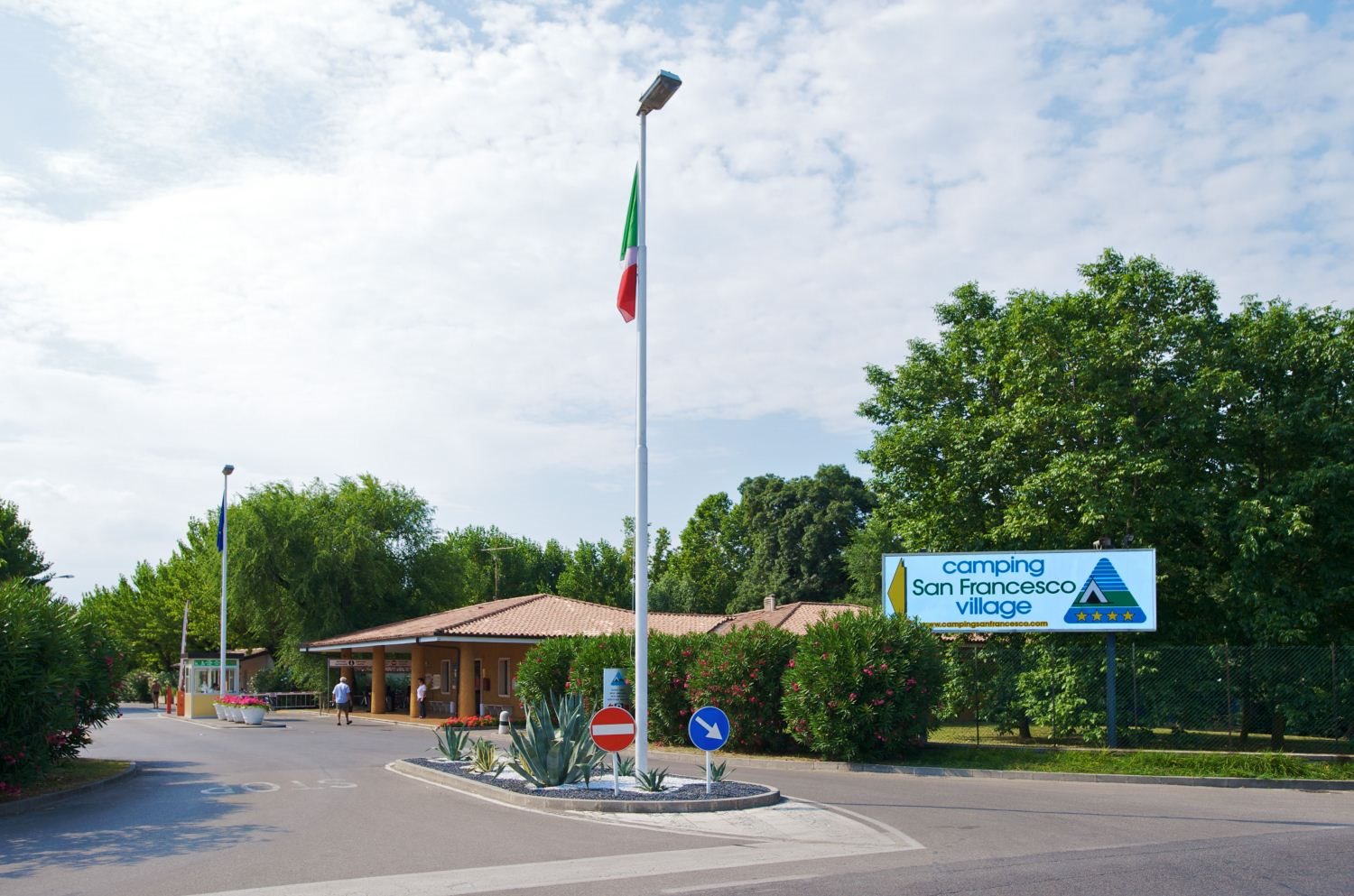 Flagpole with Italian flag standing in front of a building entrance surrounded by greenery and street signs at San Francesco