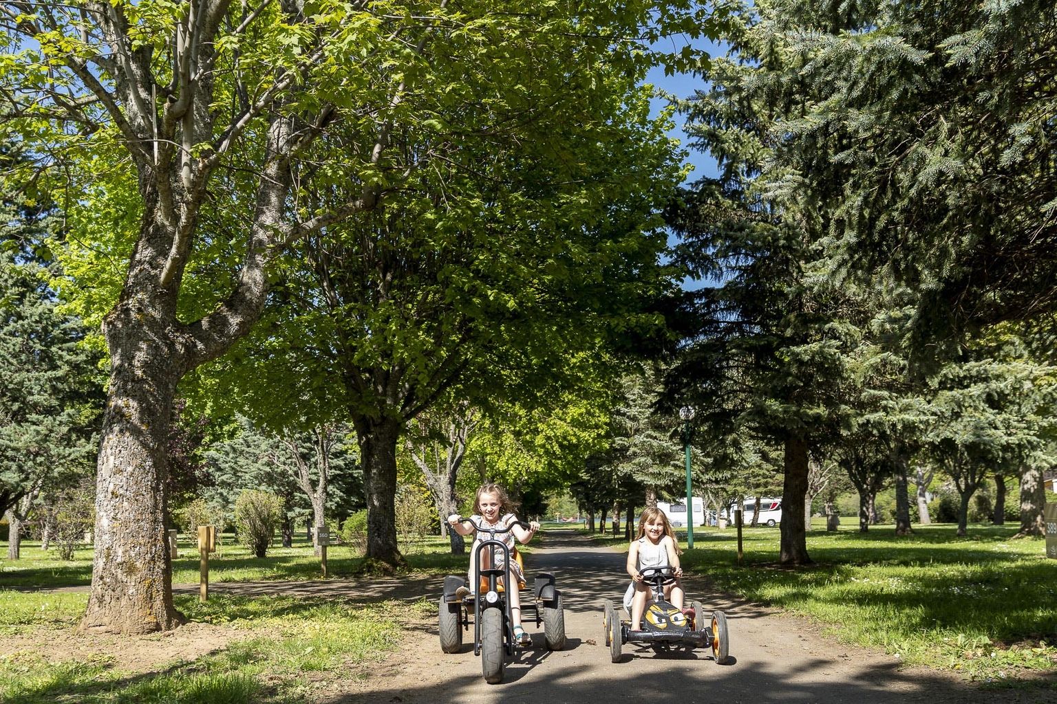 At La Ribeyre, two kids ride go-karts on a paved trail encircled by trees.