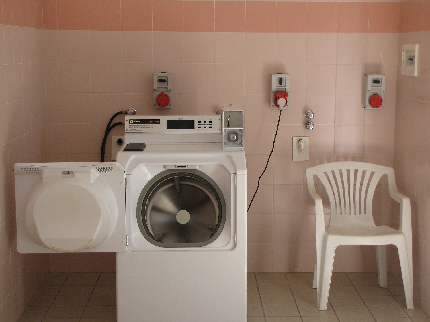 Laundry machine beside a white plastic chair in a tile-walled room for washing clothes at Belvedere Pineta