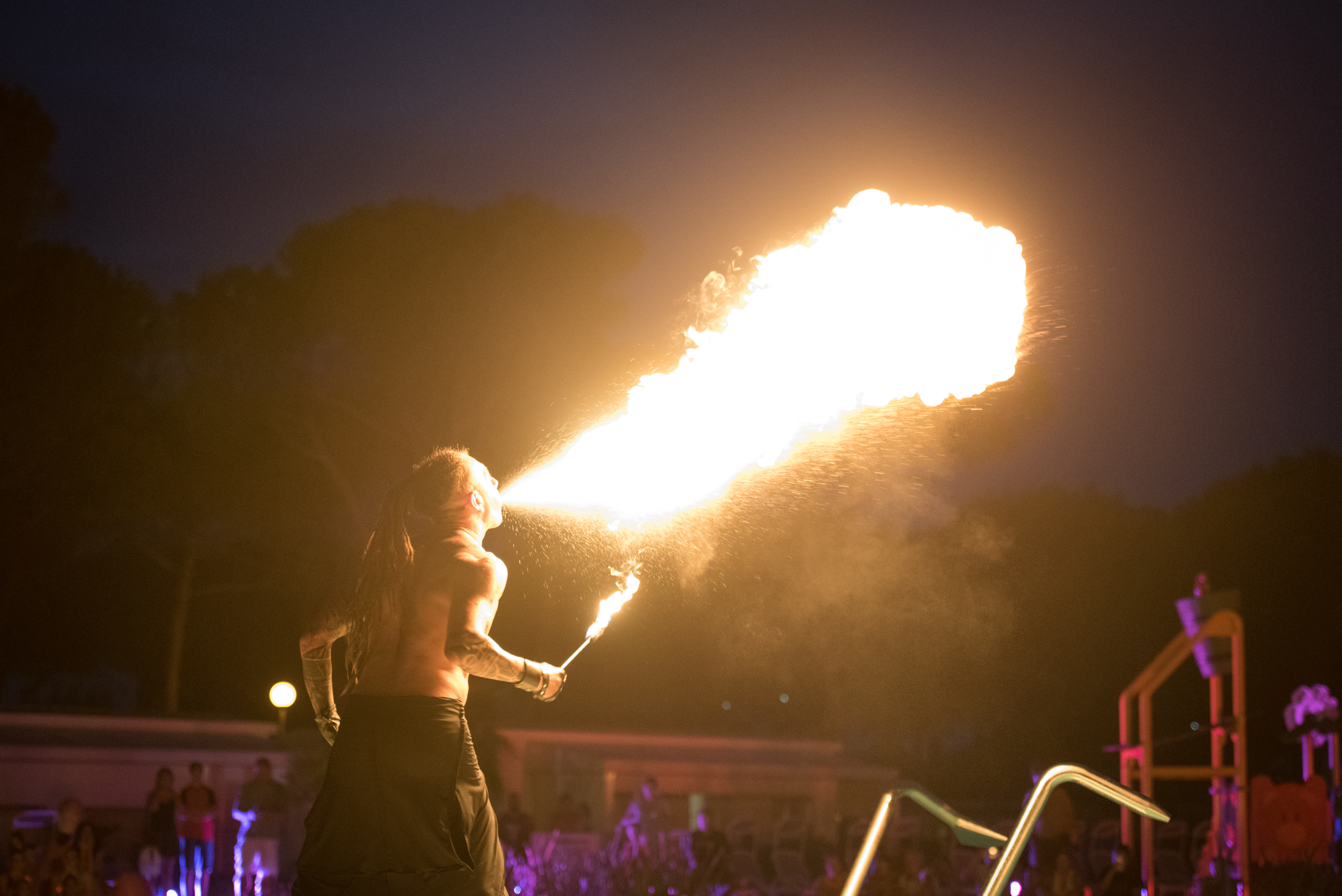 A fire-breather exhaling flames at night in front of an audience at Residence Village