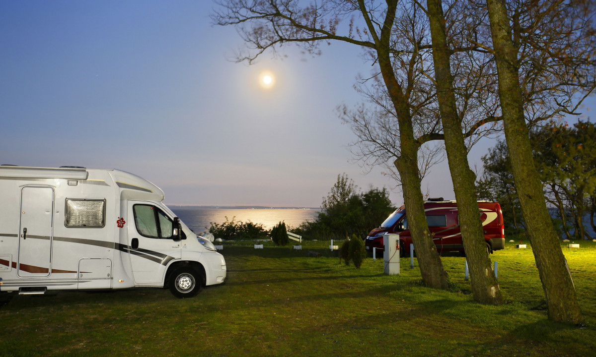 At KNAUS Campingpark Rügen, two campervans are stationed beneath trees by a moonlit ocean.