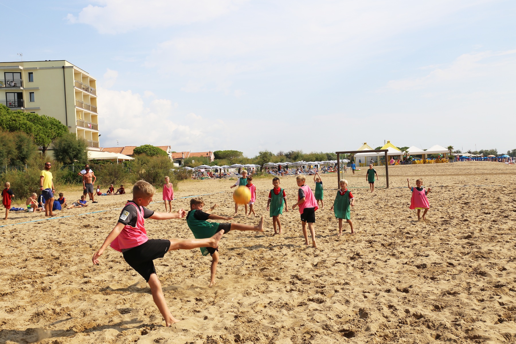 Children playing football on a sandy beach with lifeguards and sunbathers in the background at Residence Village