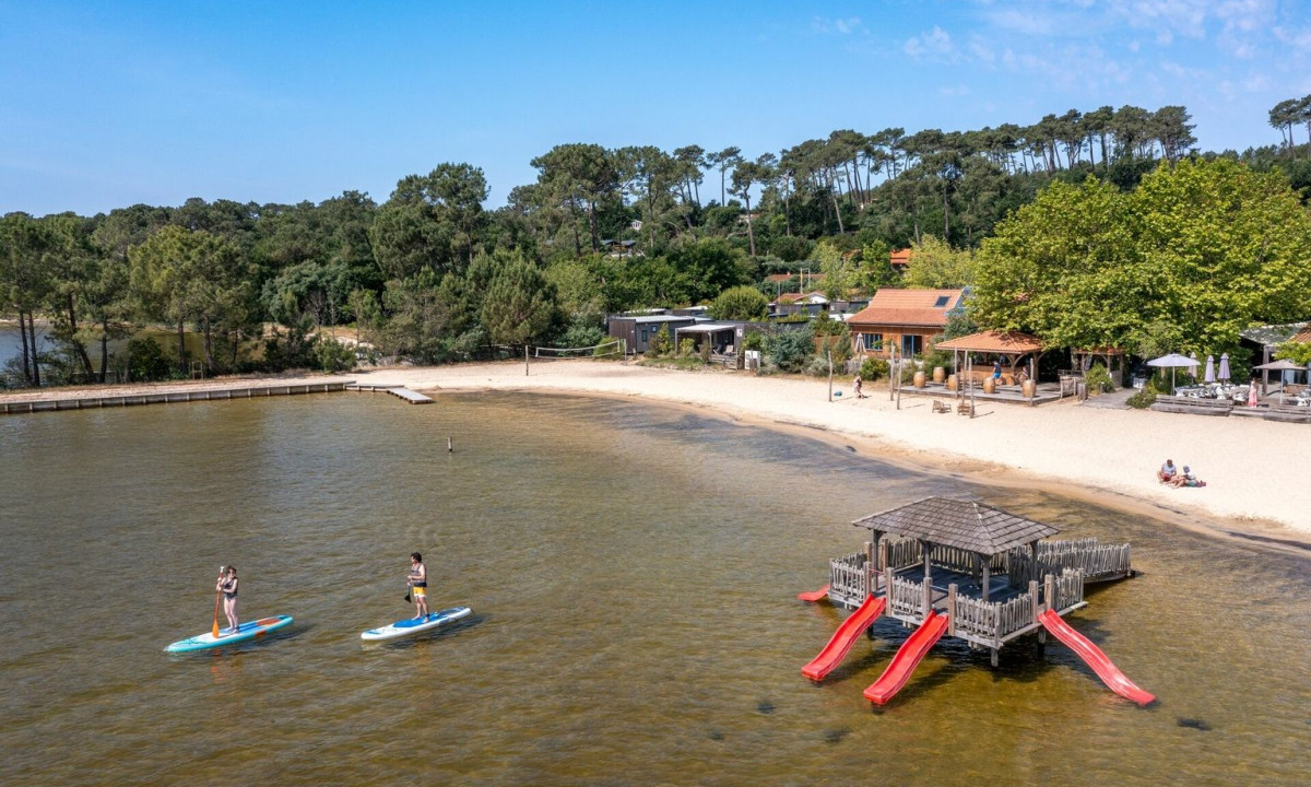 Two people paddleboarding on a lake near a sandy beach with a slide platform nearby at Maguide