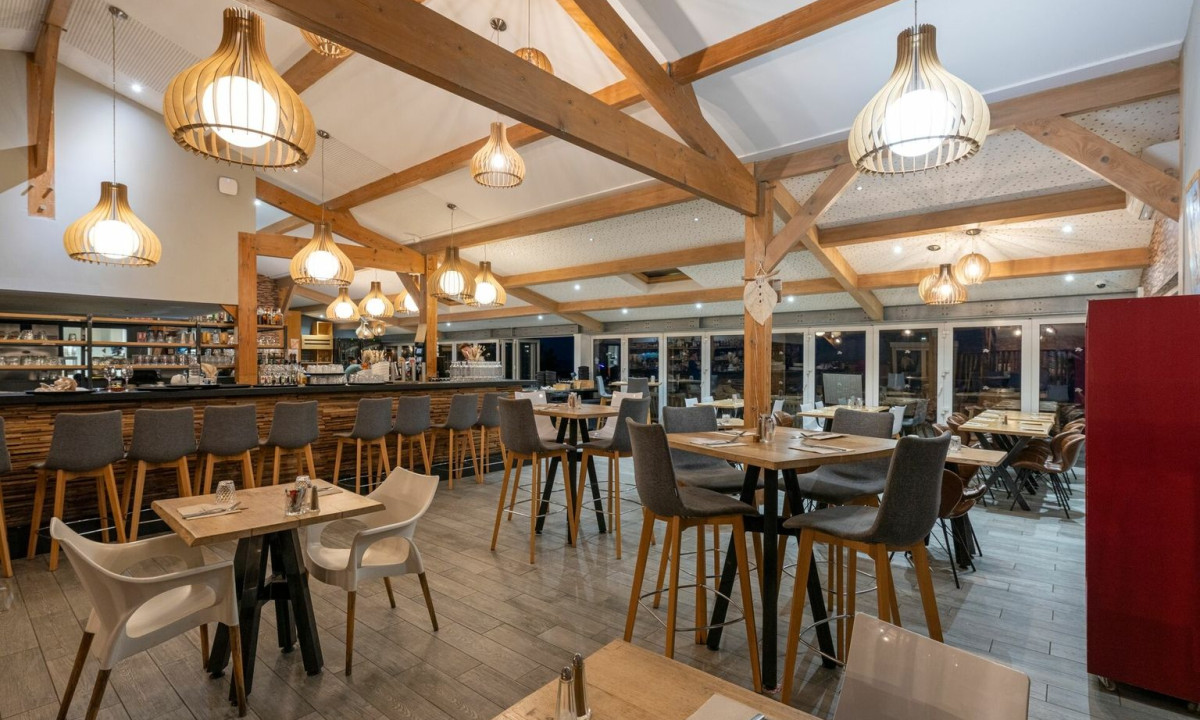 Modern restaurant with wooden beams and pendant lights, featuring a bar and seating area; cozy and inviting atmosphere at Maguide