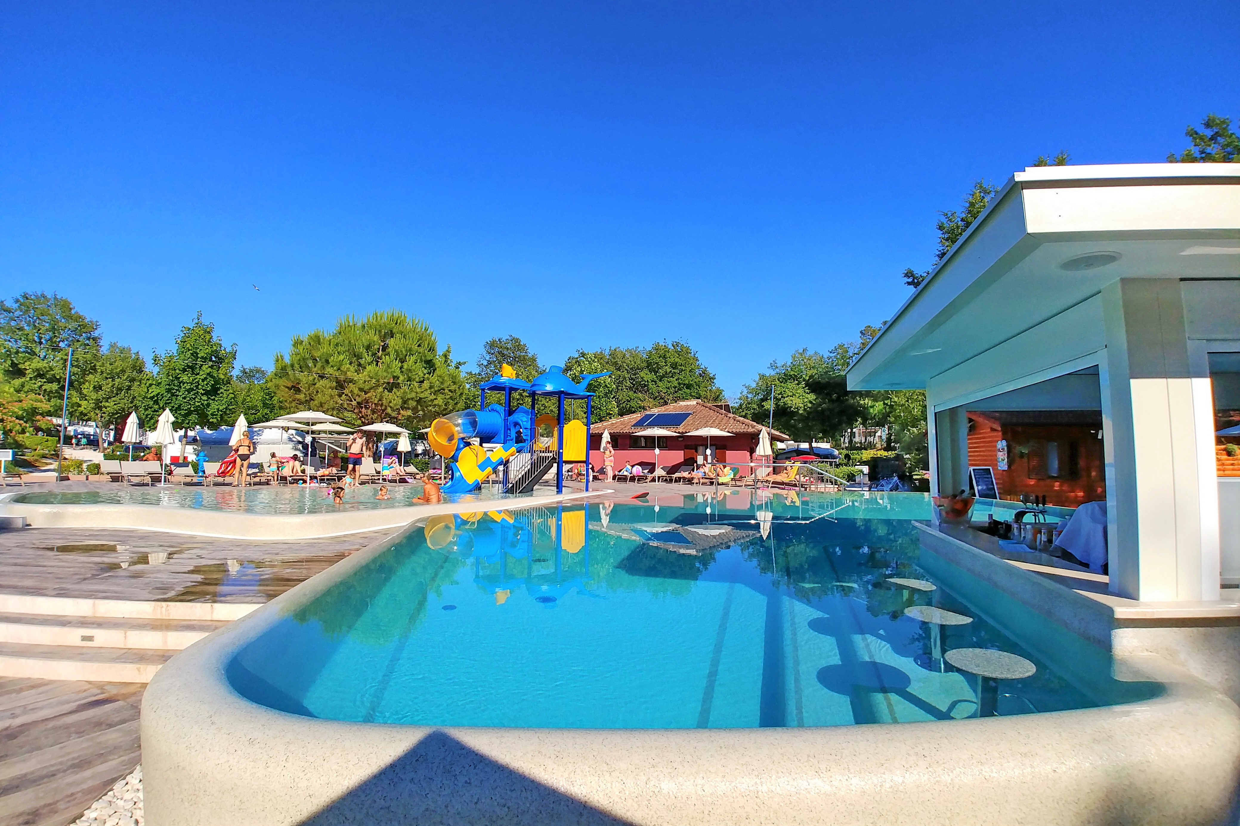 At Polidor, a pool mirrors a cerulean sky; youngsters enjoy a vibrant waterslide alongside sunbathers and parasols.
