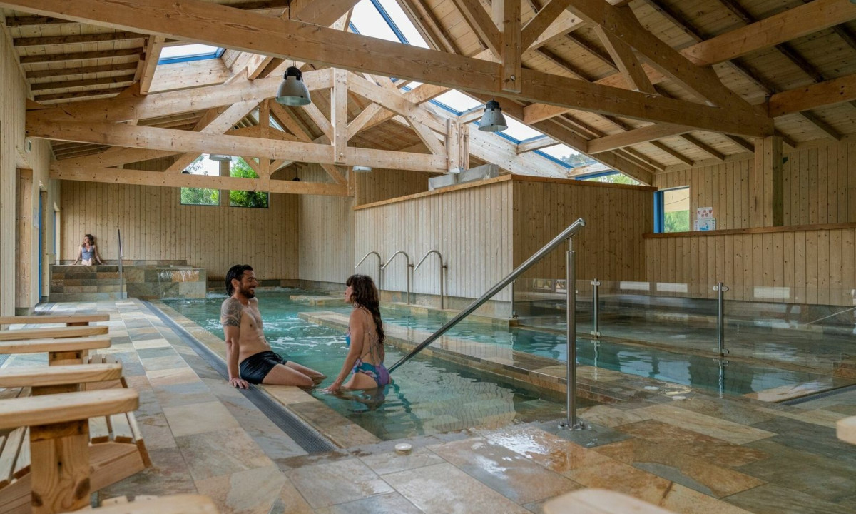 People relax in an indoor pool with wooden beam ceilings and natural light at Maguide
