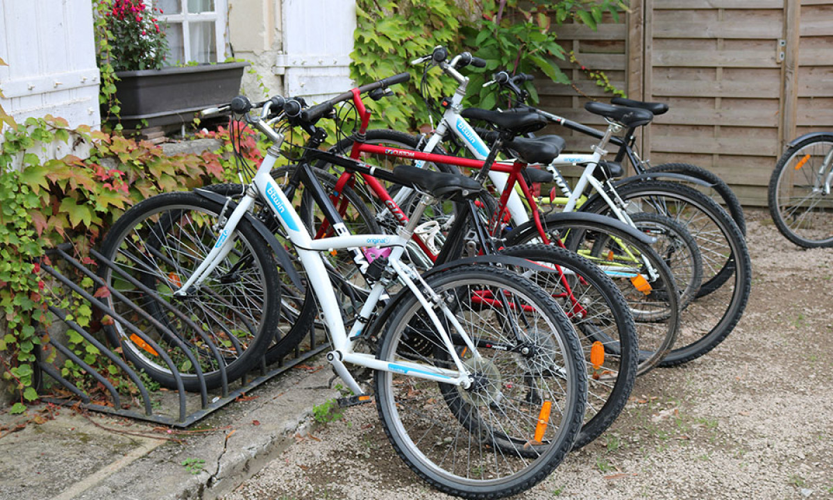At Le Petit Trianon, bicycles are secured in a rack on a gravel ground, encircled by ivy-clad walls and a wooden barrier.