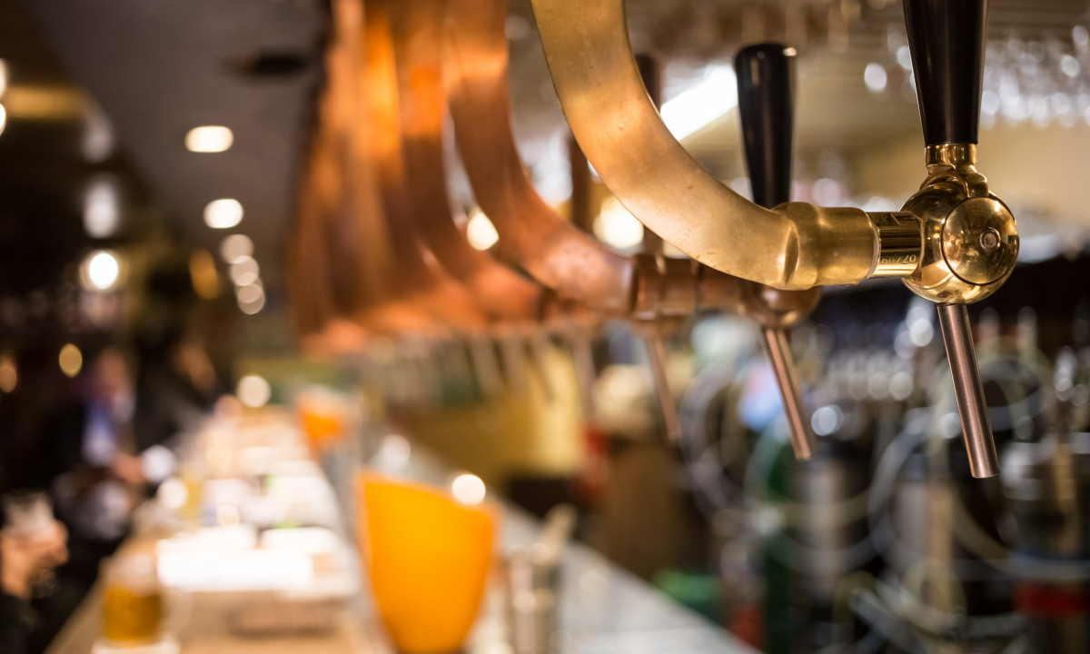 At Urban Gardens Gent, beer faucets are pouring beverages over a bar countertop in a lively indoor pub.