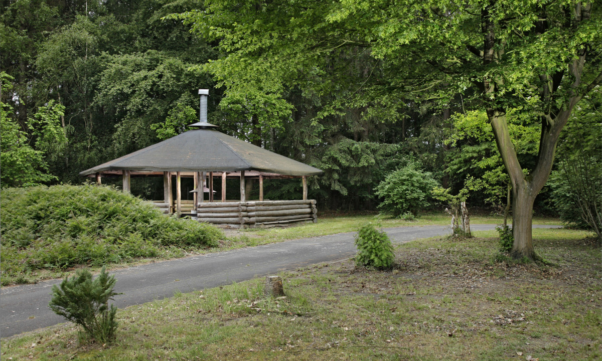 At KNAUS Campingpark Wingst, a wooden gazebo is situated amidst trees on a grassy landscape.