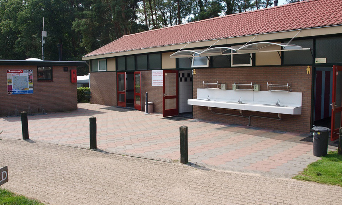 Sink area with multiple faucets mounted on a building exterior in a wooded campsite setting at de Wrange