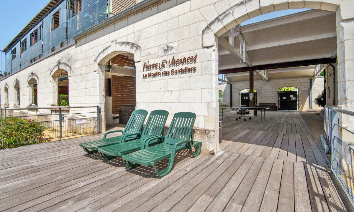 Green lounge chairs are arranged on a wooden deck next to an arched building entrance at Le Moulin des Cordeliers
