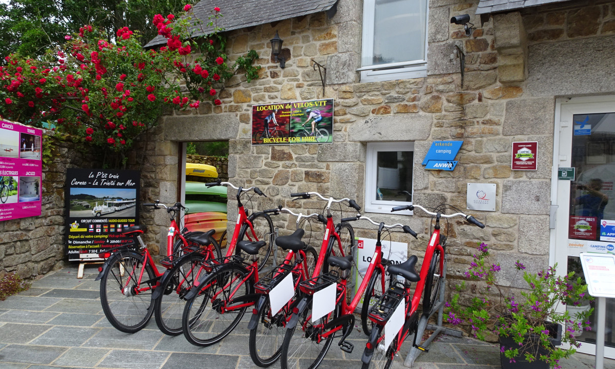 At De la Plage at the front, red bicycles are stationed in a rack, in front of a stone structure adorned with a flowering vine.