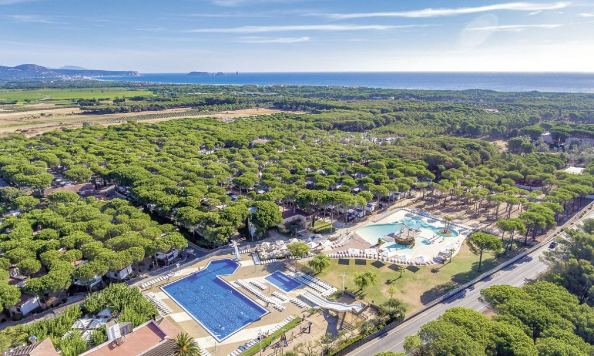 Swimming pools and buildings within a dense forest, near a road, with the sea visible in the background at Cypsela