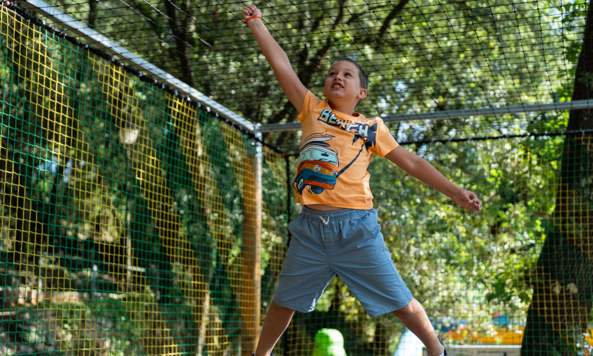 At La Clémentine, a child leaps happily on a confined trampoline, encircled by trees.