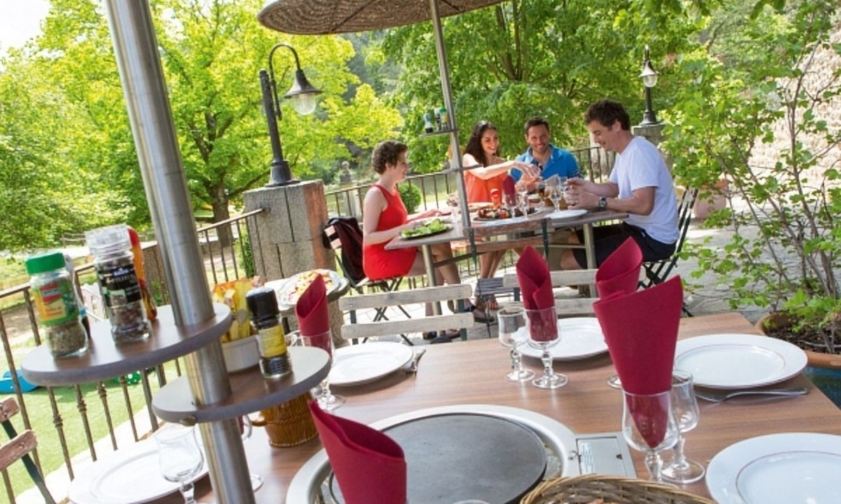 At Les Ranchisses, a table is arranged for a meal with friends dining beneath an umbrella in a vibrant, green outdoor environment.