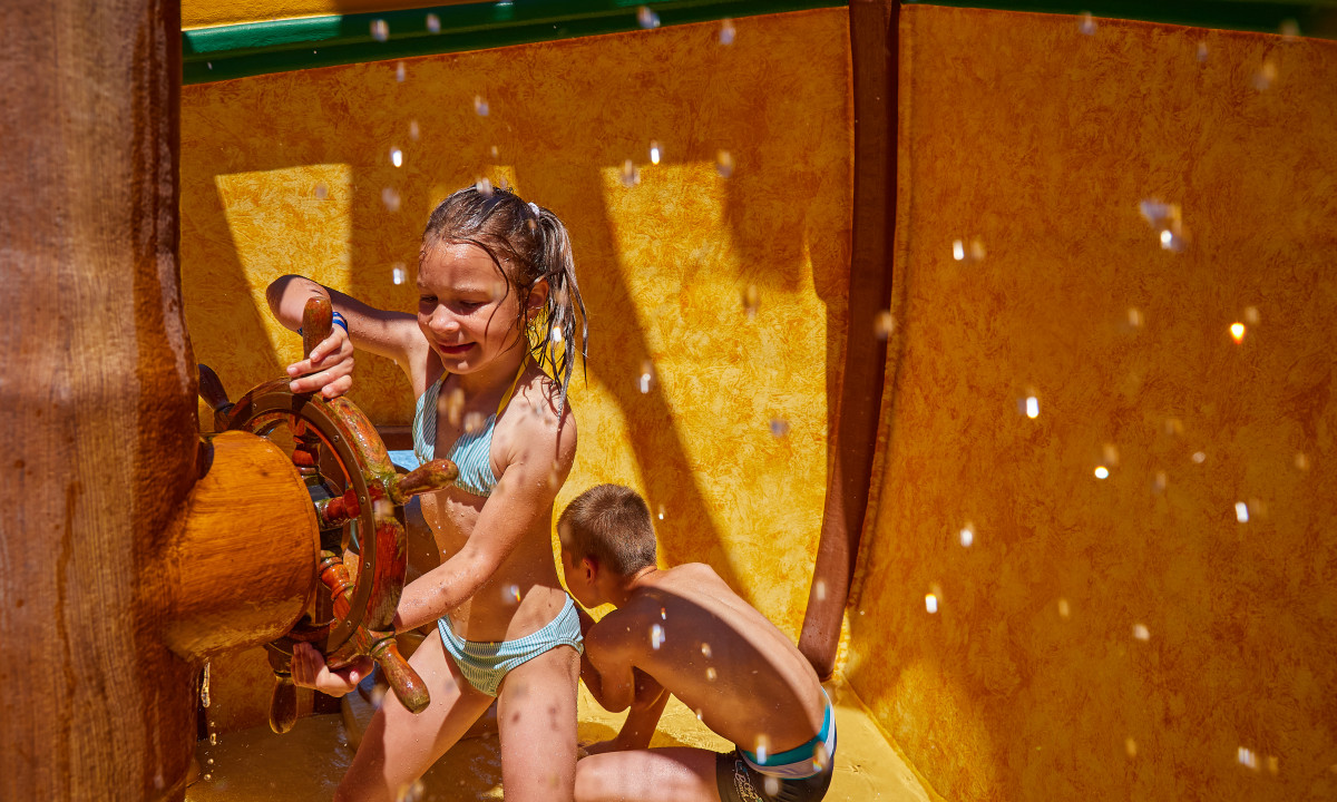At Terrasses du Lac, two kids engage with a water propeller in a vibrant yellow aquatic play zone.