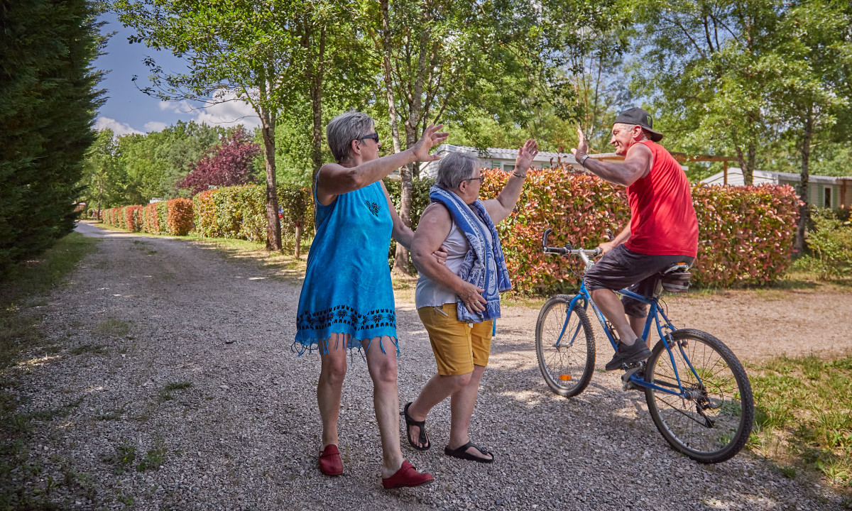 At Le Chêne Vert, two women are greeting a man cycling along a gravel trail, encircled by trees and hedges.