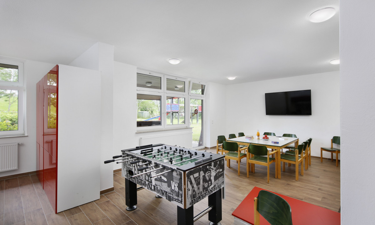At KNAUS Campingpark Eckwarderhörne, there is a foosball table in a leisure area featuring a table, seating, and a television mounted on the wall.