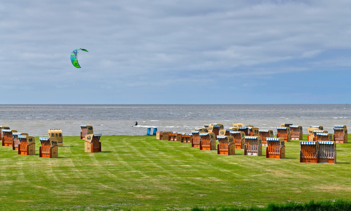 At KNAUS Campingpark Dorum, a kite surfer glides close to the coastline, encircled by many striped beach loungers on lush grass.