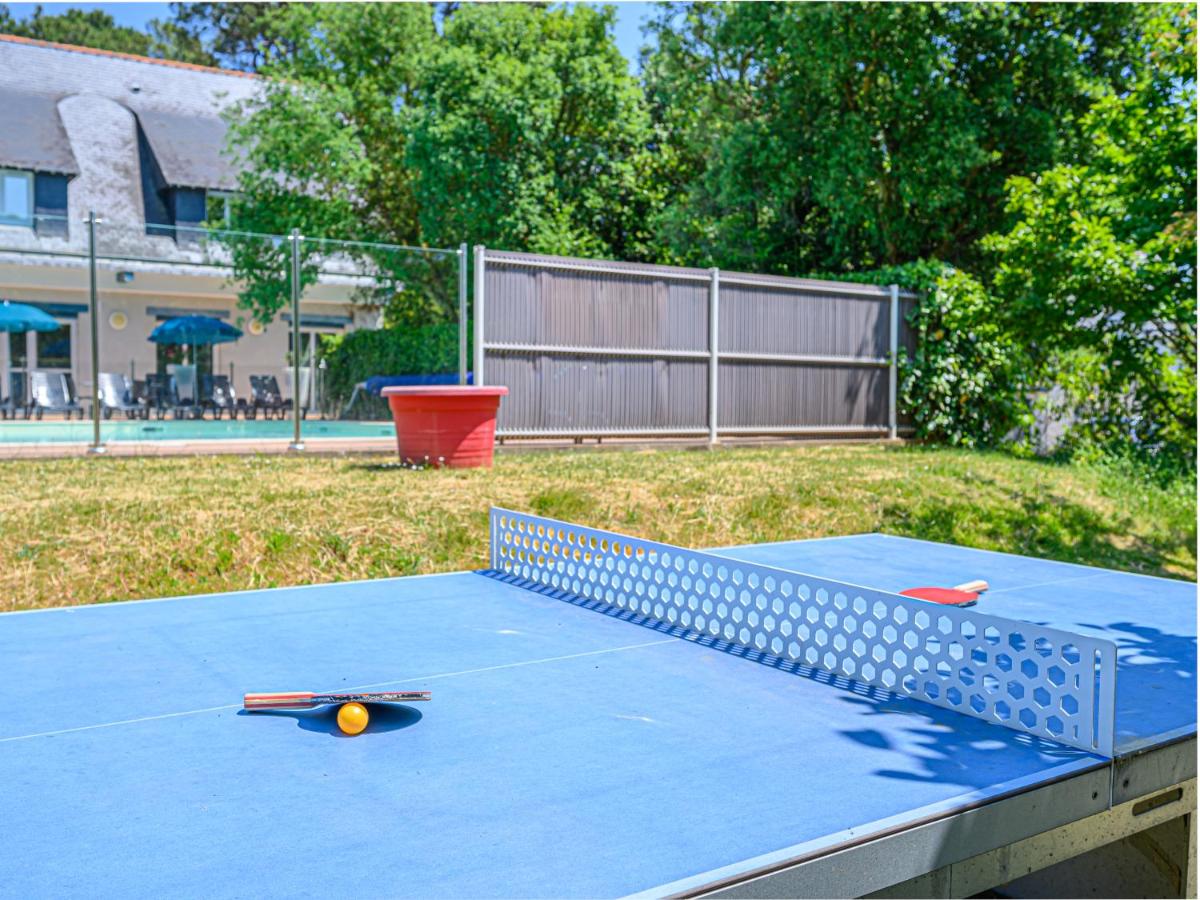 A table tennis paddle and ball rest on a table tennis table outdoors; a building and trees in the background at Ker Goh Lenn
