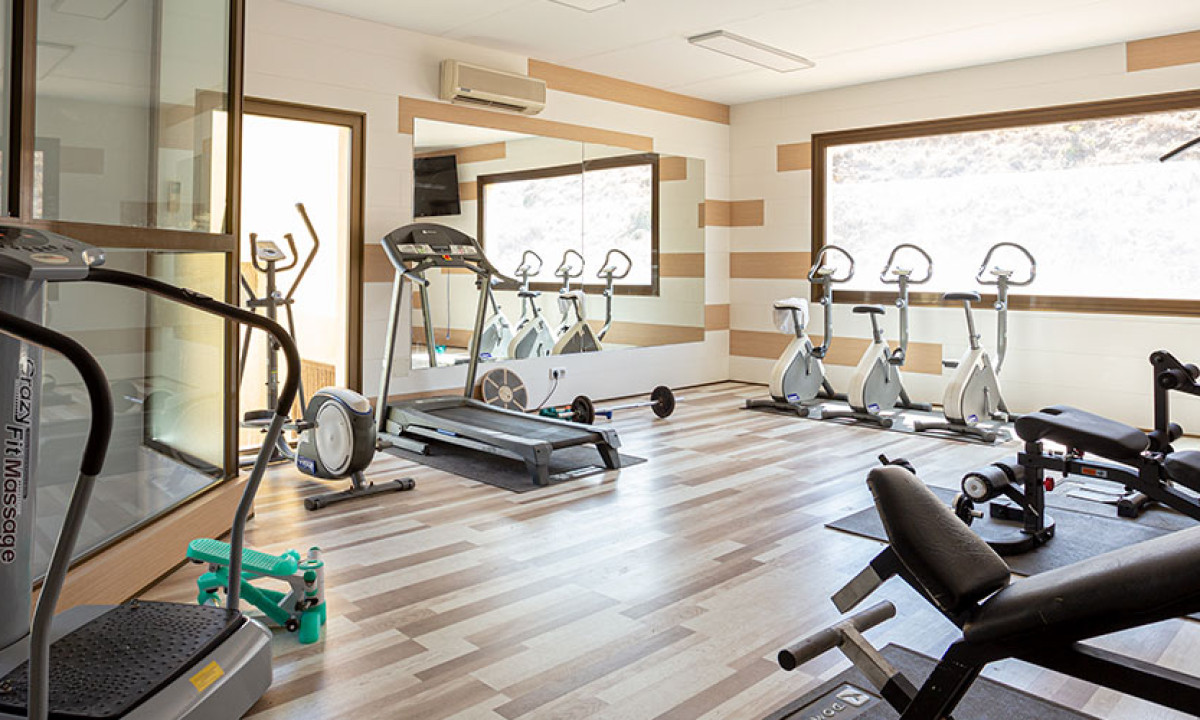 At Camping Los Escullos, a fitness center features exercise equipment organized neatly, including treadmills and stationary bicycles, in a well-lit space with large windows.