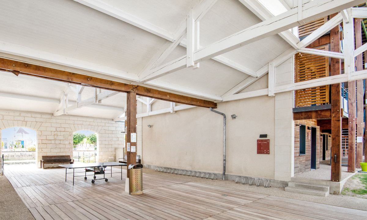 Table tennis table under a white wooden ceiling with brick arches and outdoor wooden structures at Le Moulin des Cordeliers