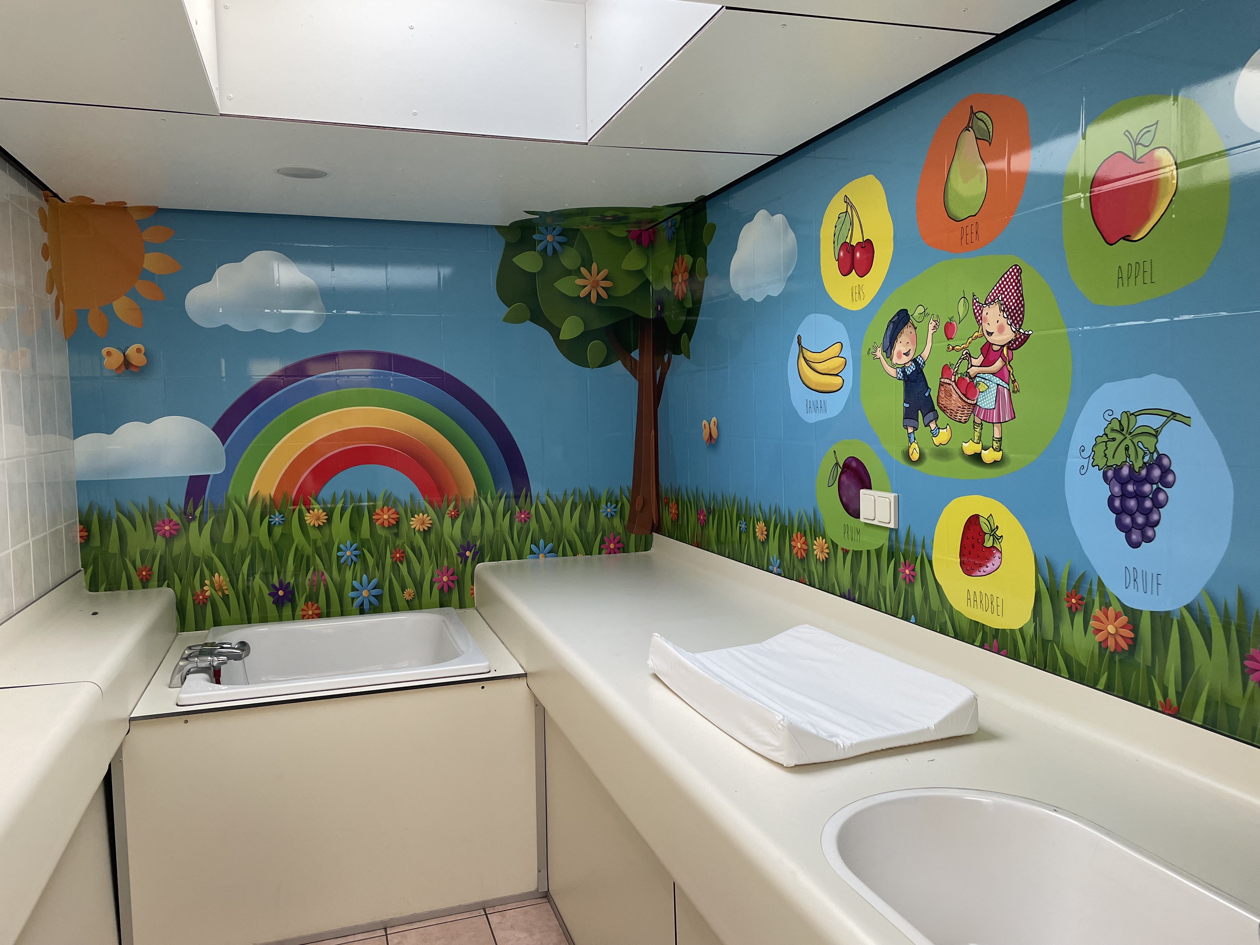 At de Vinkenkamp, a sink and changing station adorned with vibrant illustrations of a rainbow, fruits, and children in a joyful, animated style.