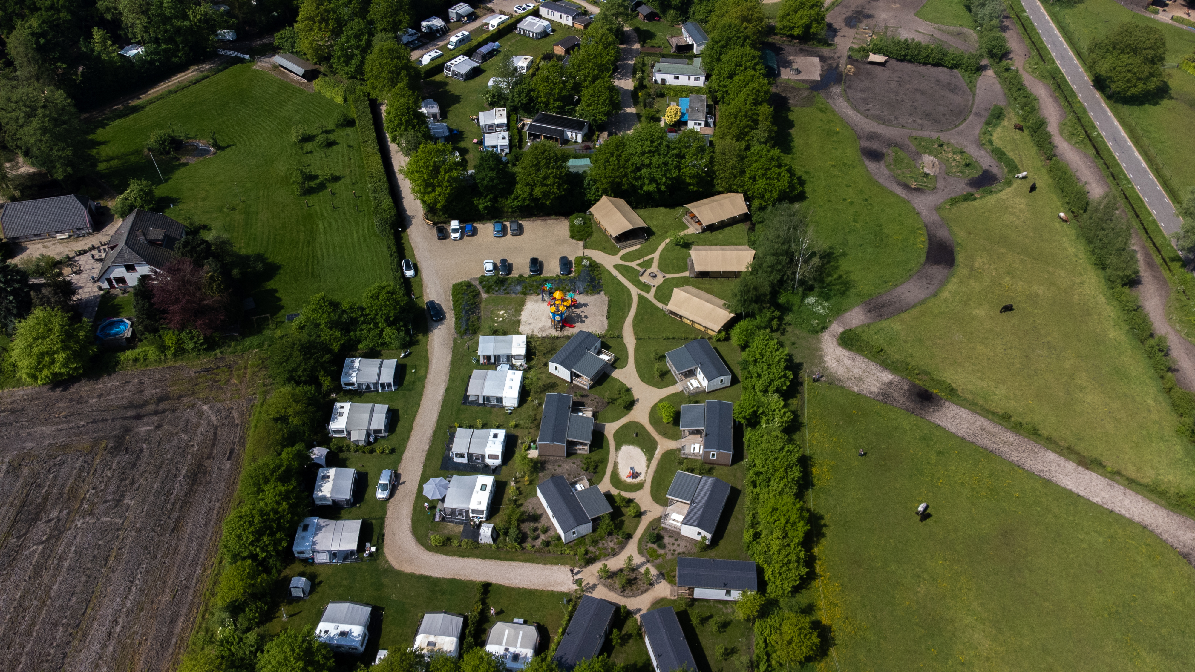 At de Vinkenkamp, an aerial perspective reveals a camping area with lodges and tents enveloped by lush vegetation, showcasing trails and a modest play area.