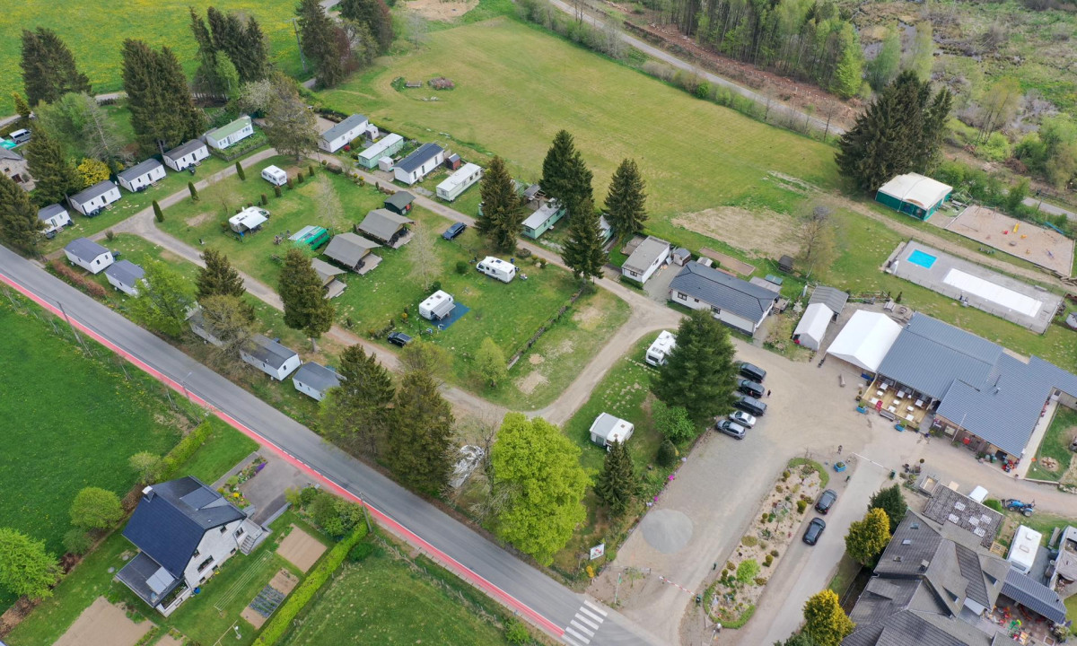 At Oos Heem, an aerial perspective reveals caravans stationed among trees and structures alongside a roadway, encircled by grassy fields.