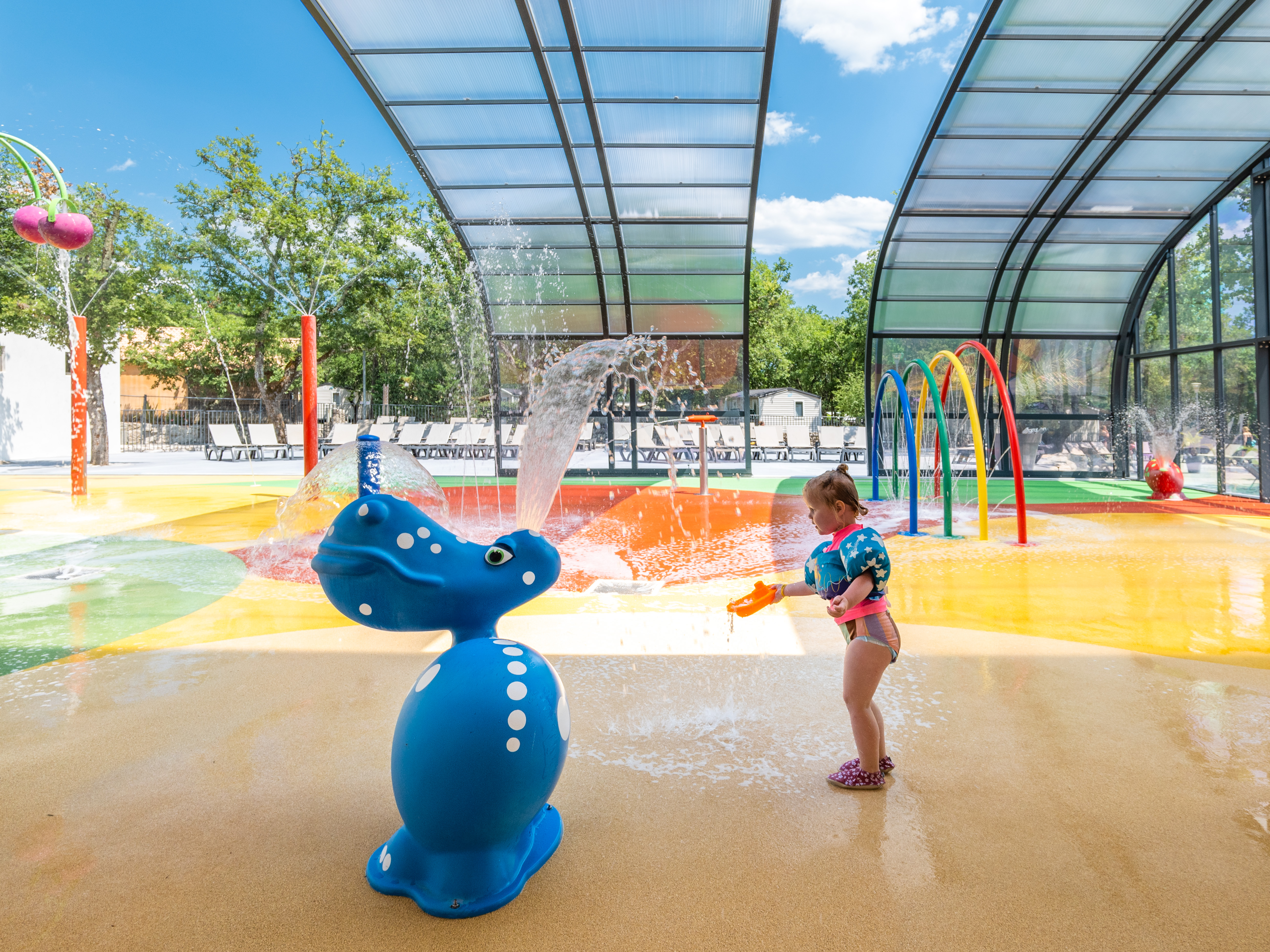 At Le Ranc Davaine, a child is enjoying a water toy amidst vibrant water jets in an indoor splash pad.