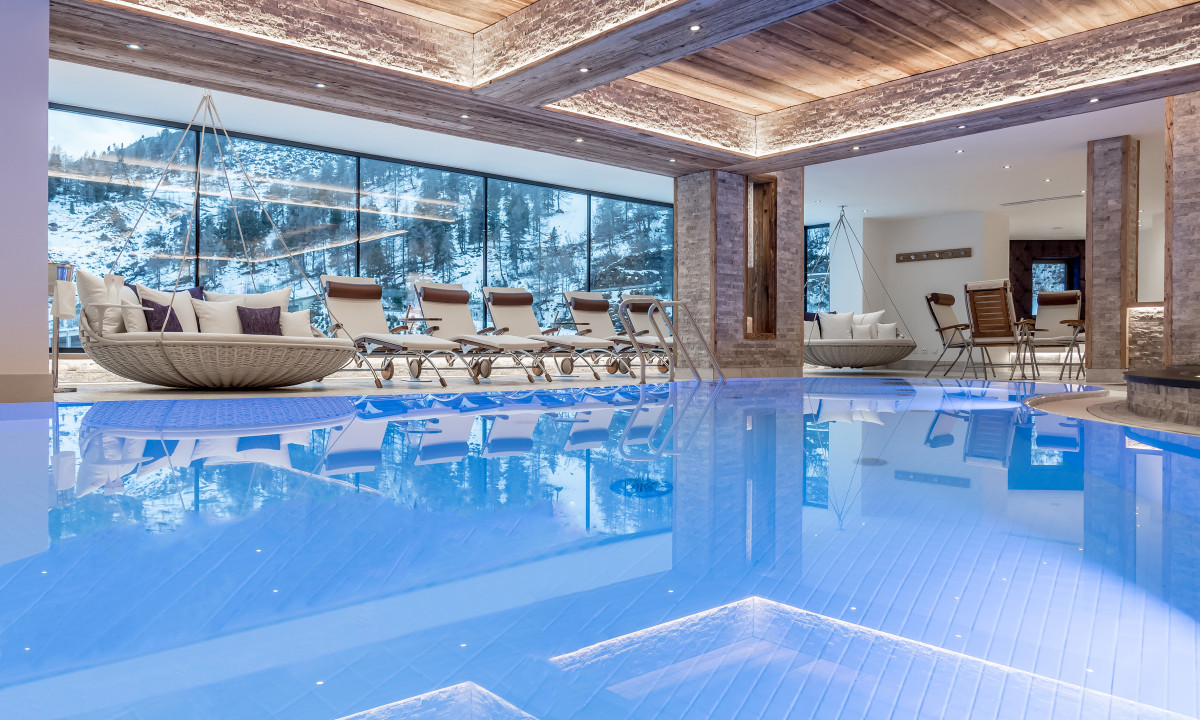 Indoor pool reflects cozy seating area and snowy mountain view through large windows, creating a serene atmosphere at Kesselspitze Valamar Collection Hotel