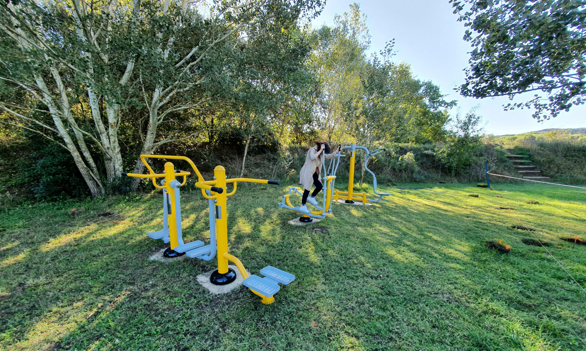 At La Sousta, outdoor exercise apparatus is being utilized by an individual in a grassy, tree-dense camping area.