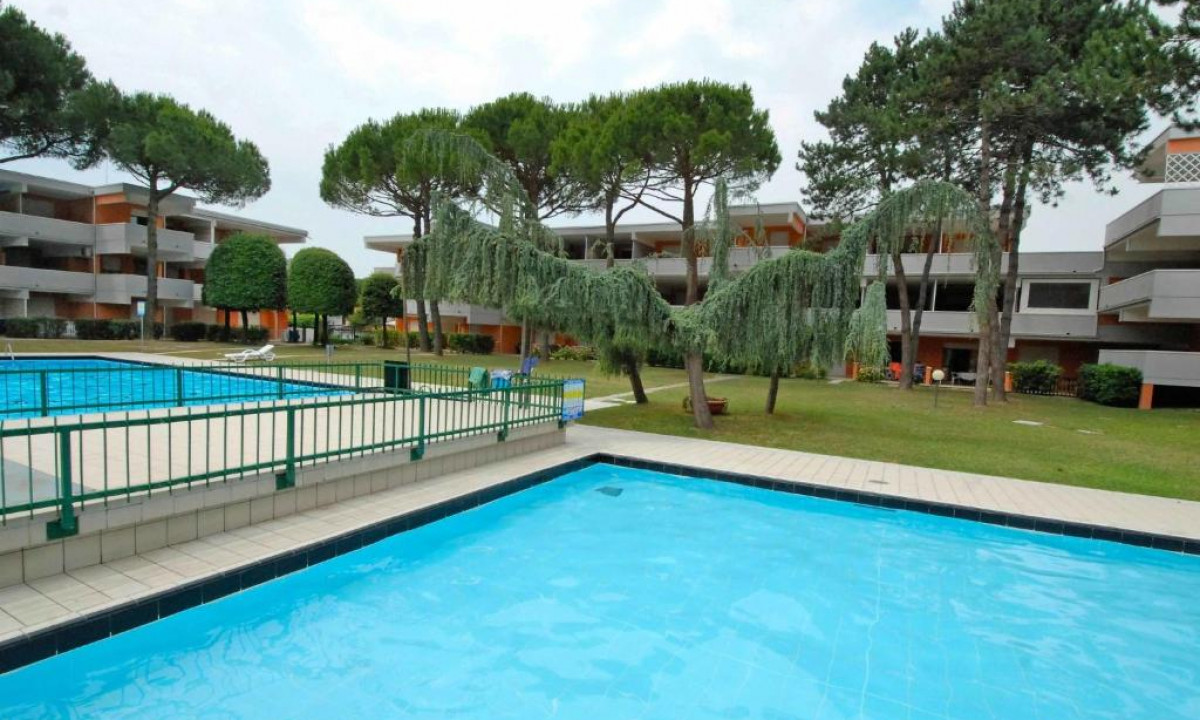 Swimming pool surrounded by green fence, set in front of modern building complex with trees and lawn at Solarium