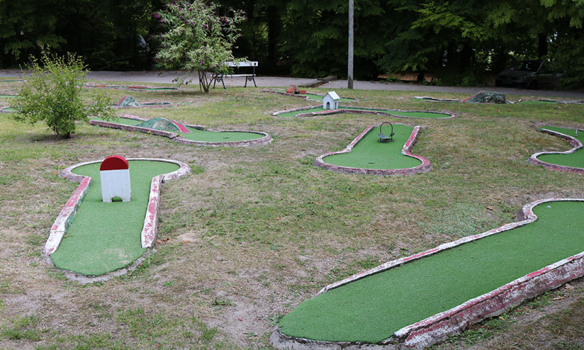 At Le Petit Trianon, there is a mini-golf course featuring obstacles, located in a grassy area encircled by trees.
