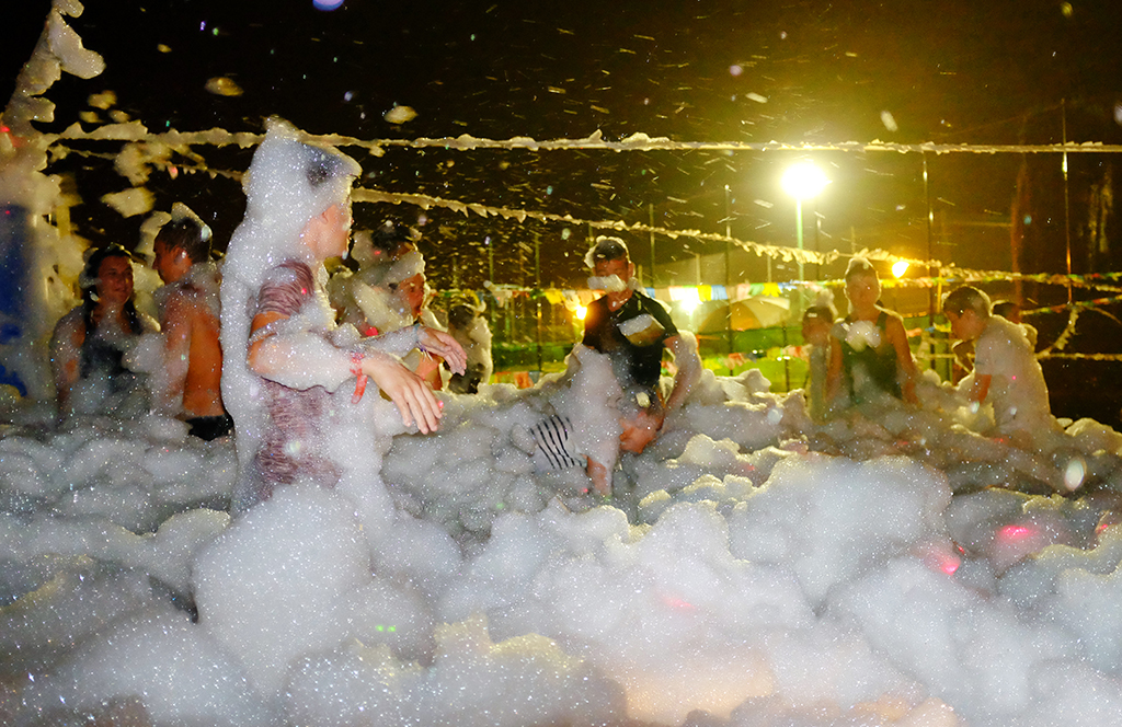 People play in soap foam bubbles at night under strings of lights at El Pinar