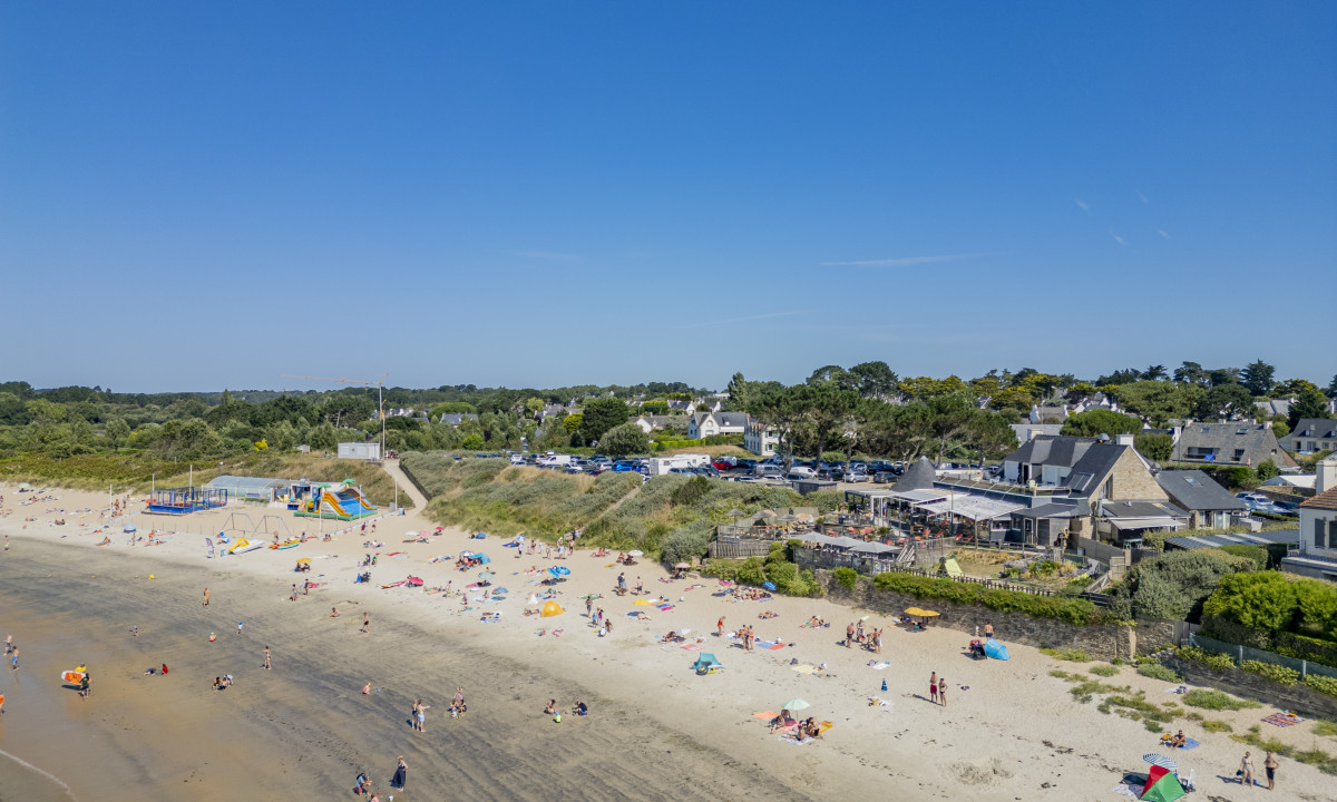 At De la Plage, sunbathers unwind on the sandy beach, with residences and lush vegetation in the backdrop.