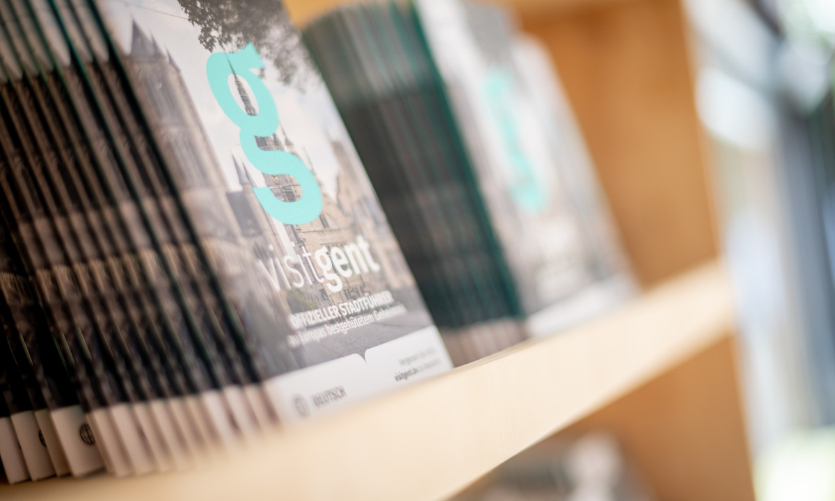 At Urban Gardens Gent, brochures showcased on a wooden shelf provide travel details in a tourist information center.