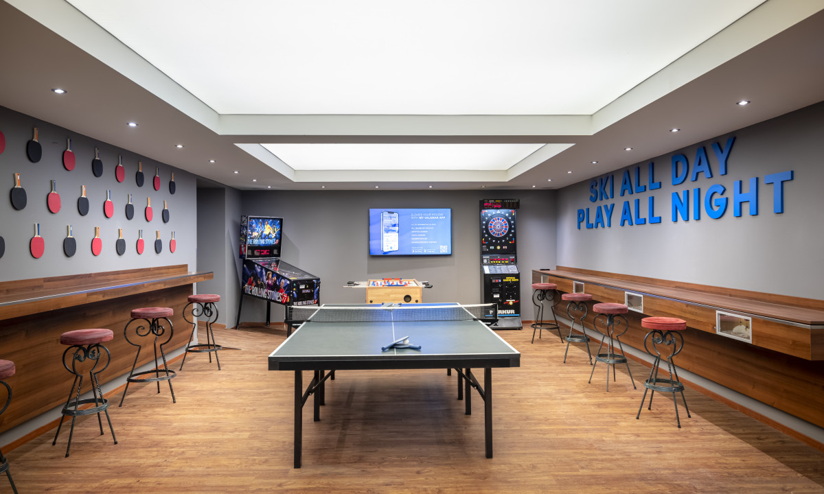 Table tennis setup stands idle in a game room, featuring vintage arcade machines and bar-style seating at Kesselspitze Valamar Collection Hotel