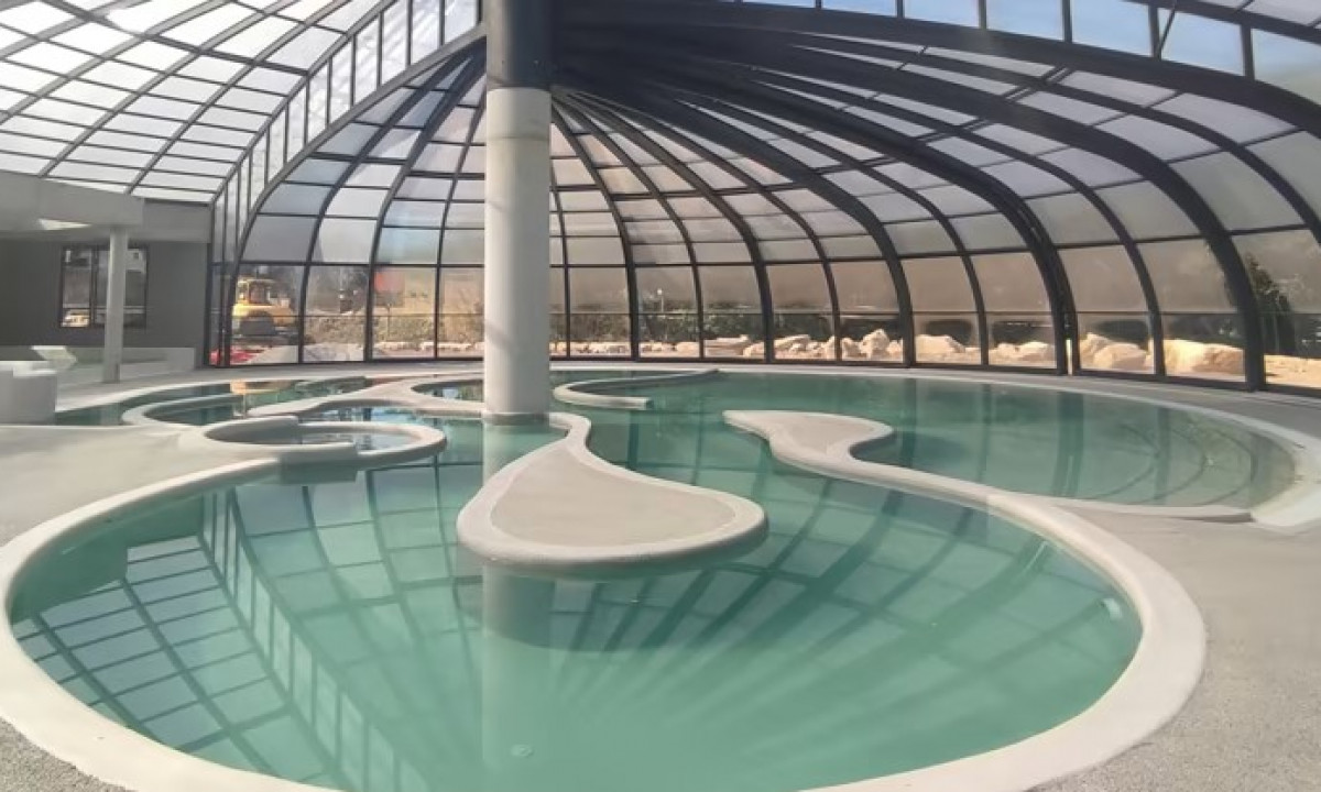 At Les Ranchisses, there is an indoor swimming pool featuring a winding design, enclosed by a glass dome structure and bordered by relaxation areas.