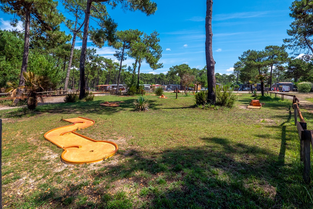 At Marvilla Parks Atlantic Club Montalivet, a miniature golf course is situated on a grassy landscape, encircled by trees and camper vans, beneath a clear blue sky.