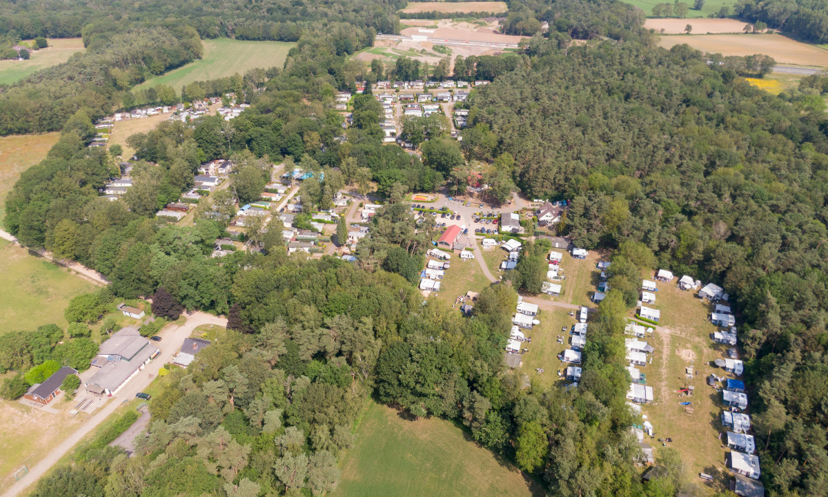 Aerial view of numerous trailers and RVs parked amidst dense trees and open fields at de Wrange