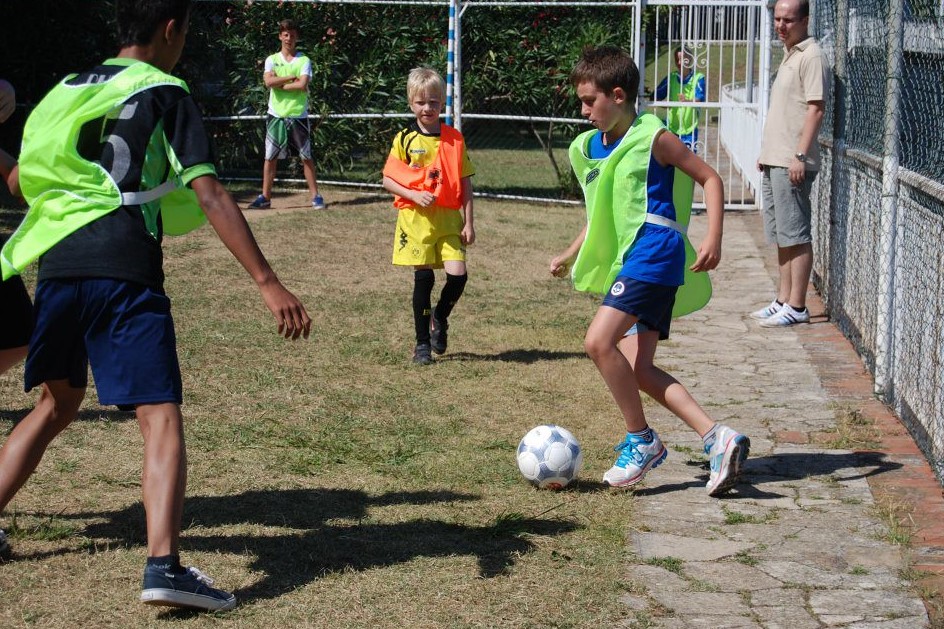 Children play soccer on a grassy field while adults watch from the sidelines at Sant' Anna Residence