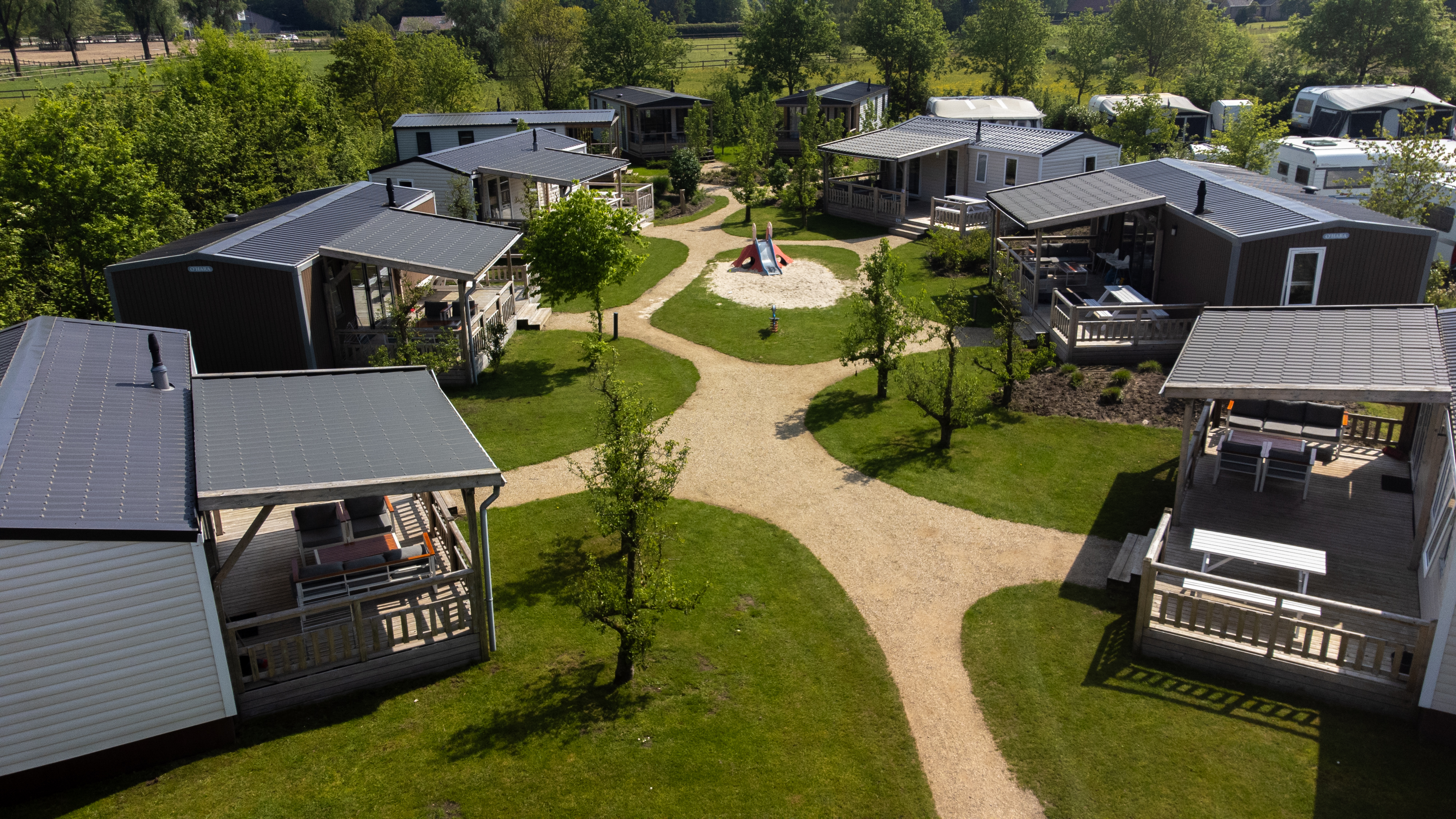 At de Vinkenkamp, cottages with verandas encircle a central play area on a grassy field, linked by meandering pathways.